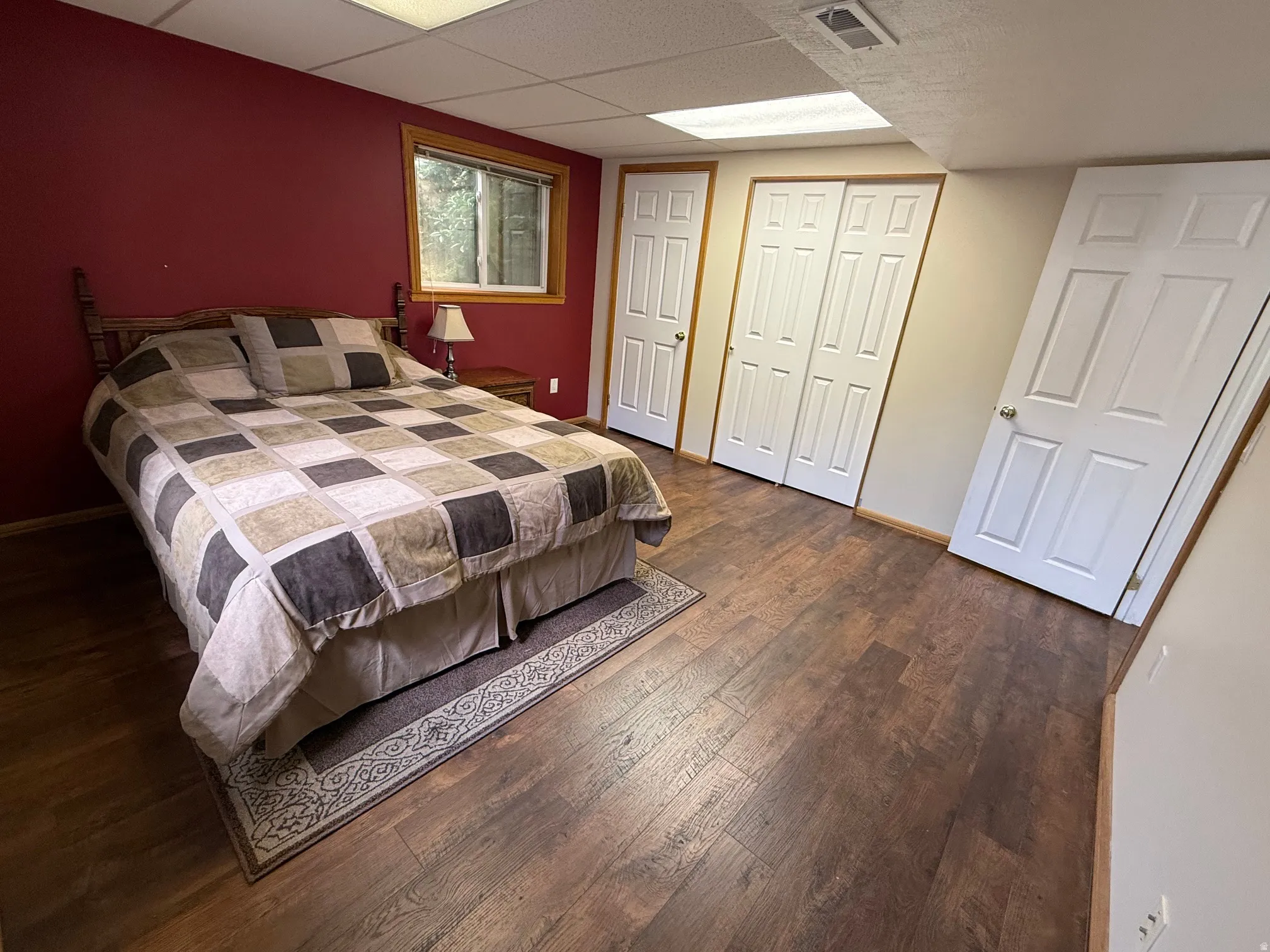 Bedroom featuring wood-finish flooring, a window with natural wood trim, and multiple white paneled doors