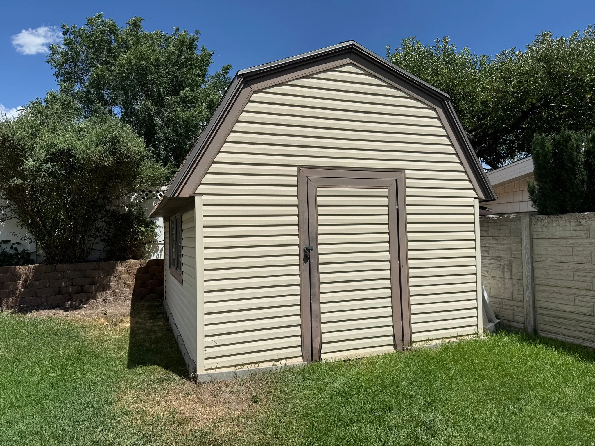 Gable-roof shed featuring beige horizontal siding, dark trim, and a single entry door