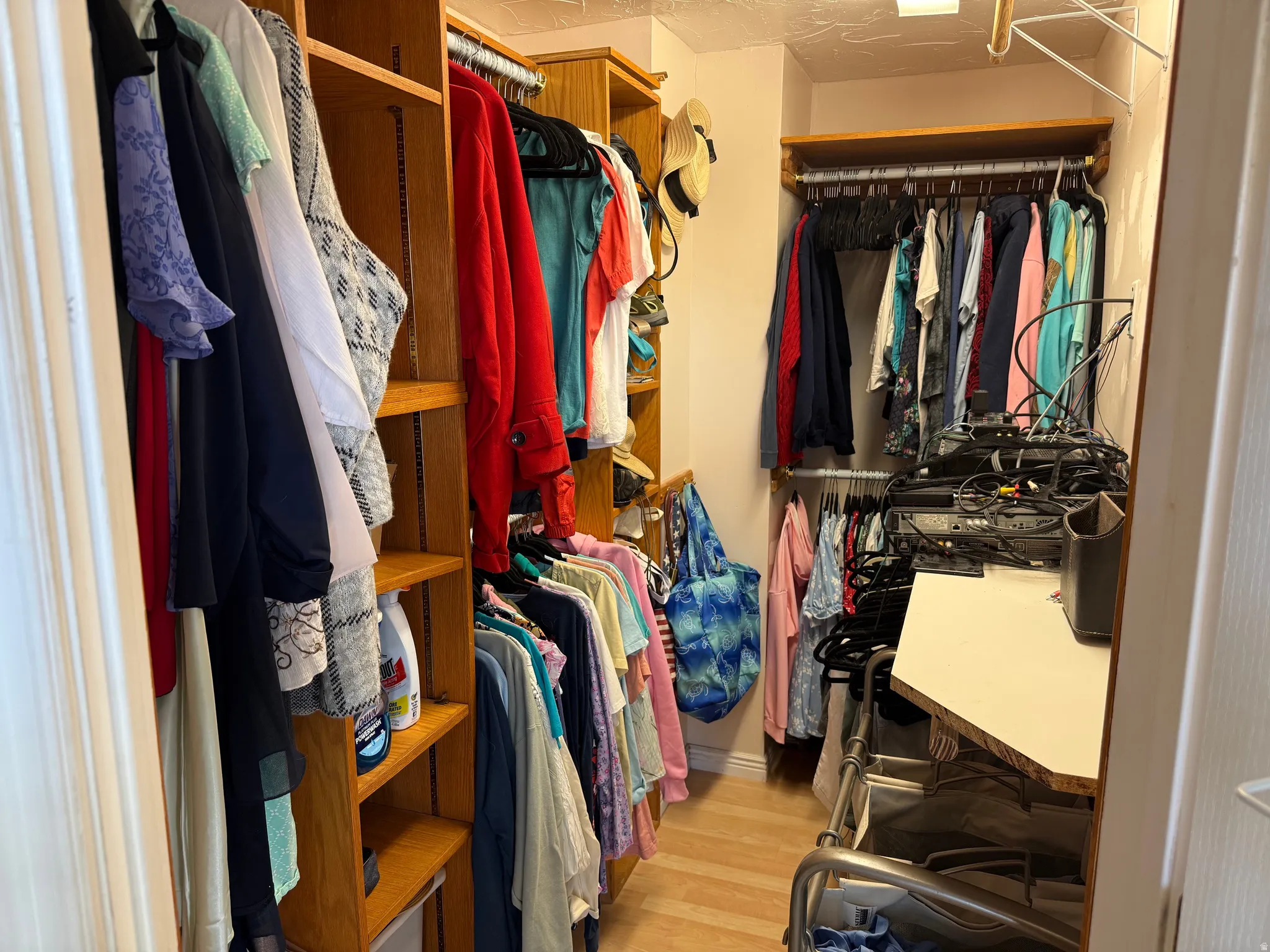 Walk-in closet featuring extensive built-in shelving, multiple hanging rods, corner desk surface, and wood-finish flooring