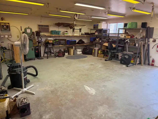 Spacious multi-purpose workshop featuring a concrete floor, extensive overhead fluorescent lighting, built-in shelving, heat and A/C, dust collection system and a window