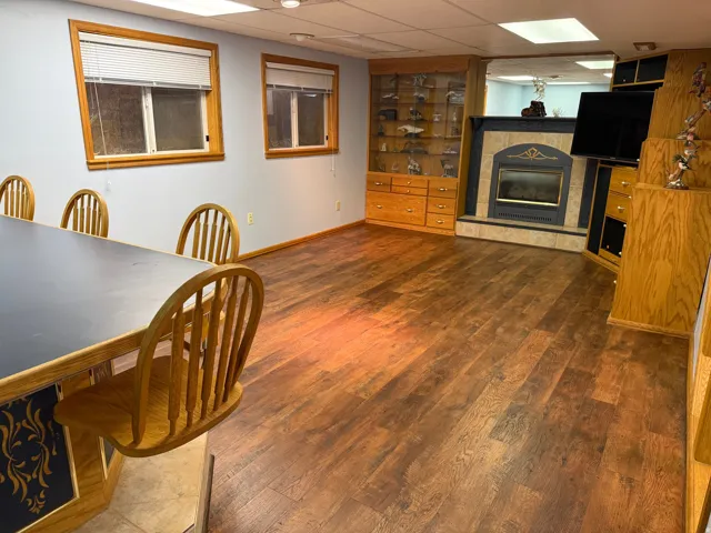Spacious room featuring wood-finish flooring, light blue walls, and two windows with wood trim, fireplace.