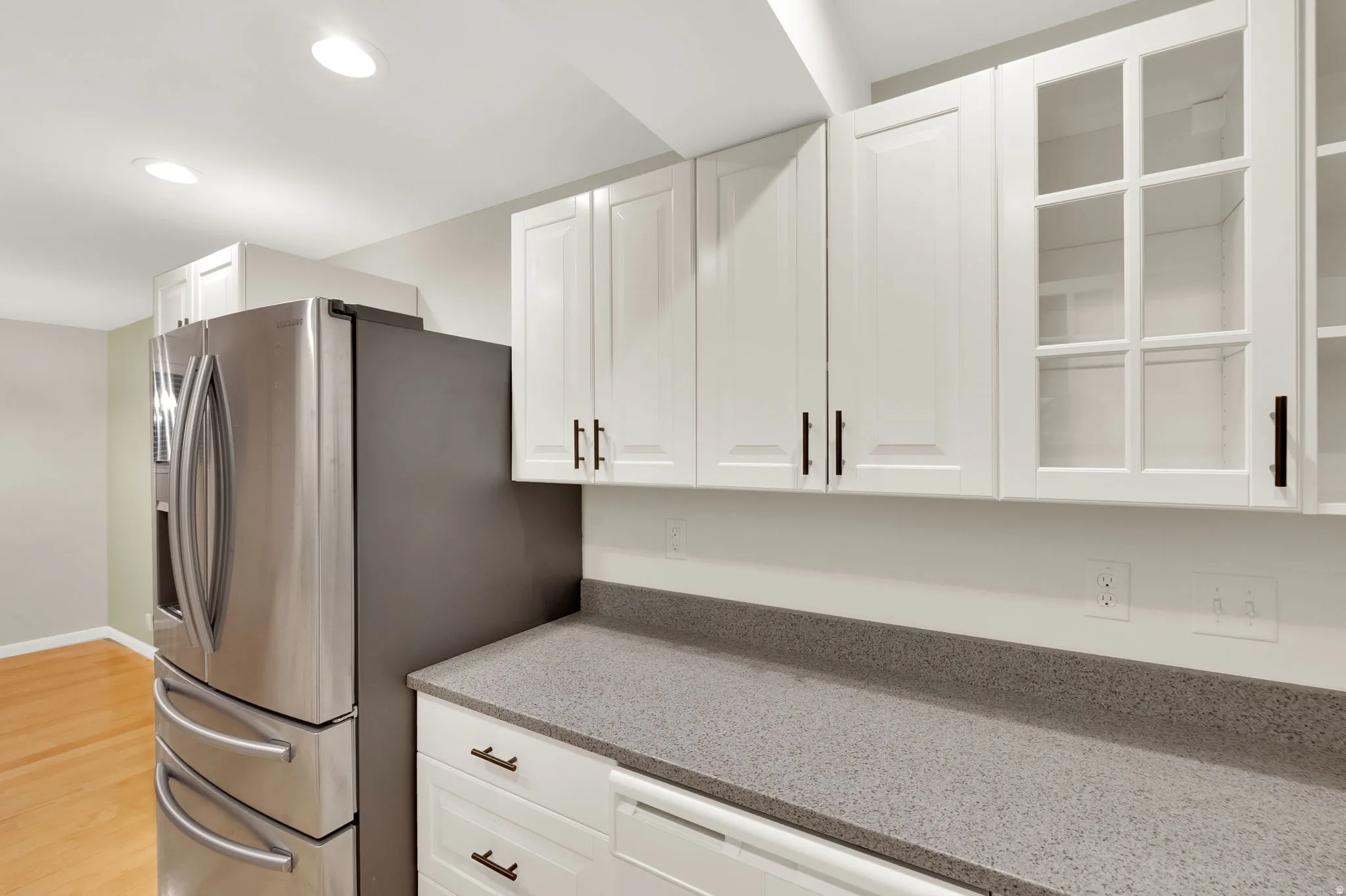 Kitchen featuring white shaker cabinetry with black hardware, a grey speckled countertop, integrated stainless steel refrigerator, and recessed lighting
