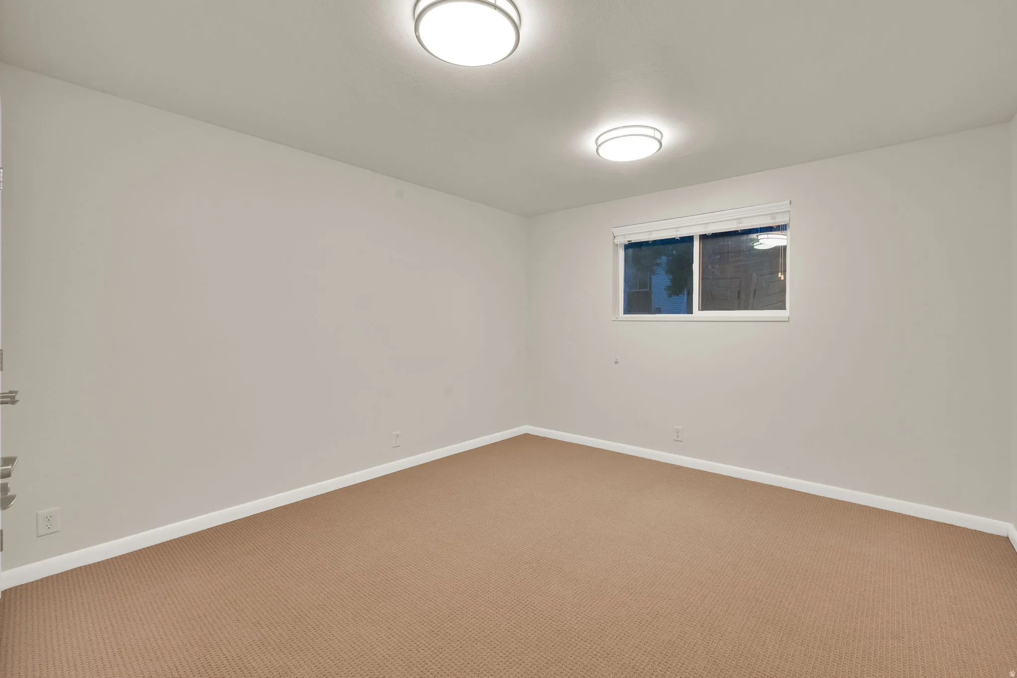 Carpeted interior space featuring a window with white blinds, two ceiling-mounted flush light fixtures, and neutral wall tones