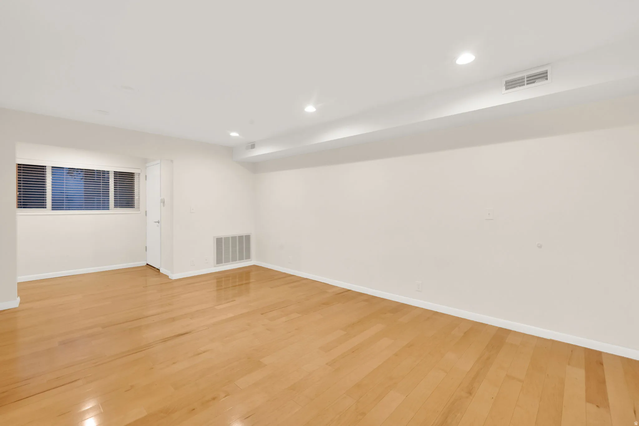 Hardwood flooring spans this room, featuring recessed lighting, a white painted door, and a built-in ventilation grate