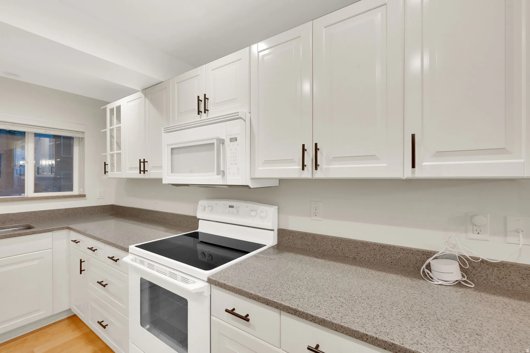 Modern kitchen featuring abundant white cabinetry with dark hardware, stone-finish countertops, and an integrated white microwave