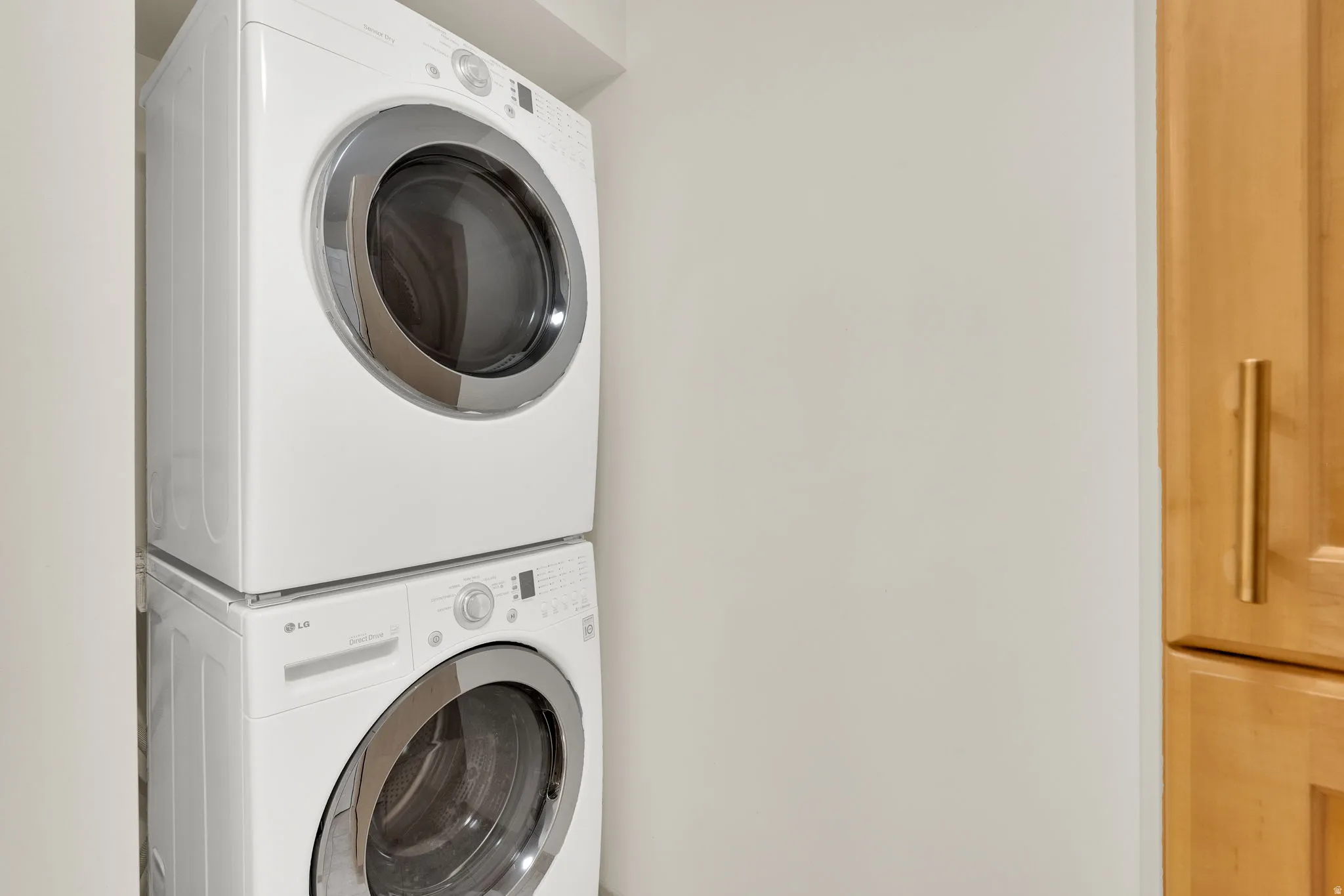 Stackable white front-loading washer and dryer units, complemented by light wood-finish cabinetry with linear gold-tone hardware
