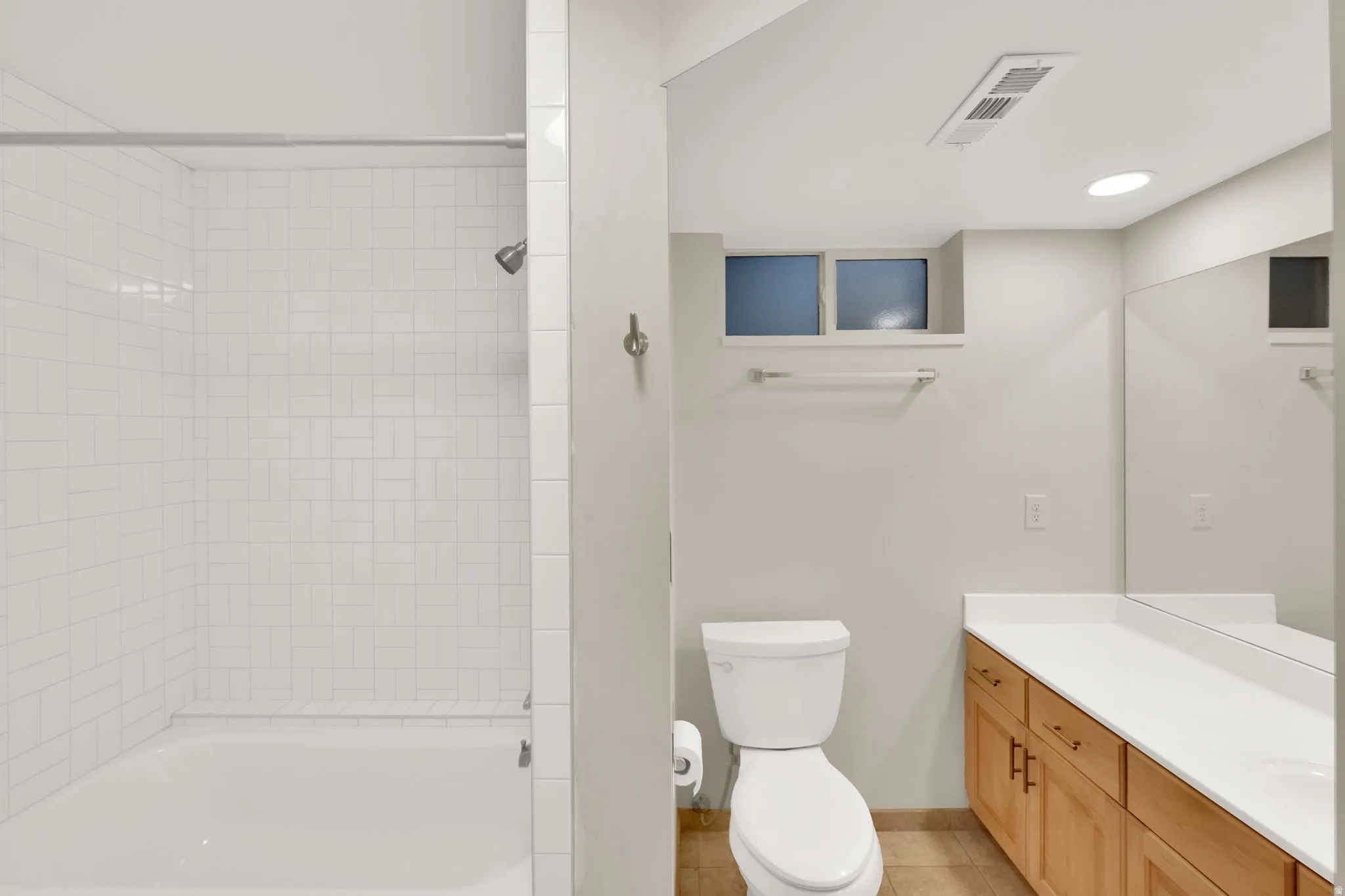 Bathroom featuring a white subway-tiled shower/tub combination, a toilet, a light wood-finish vanity with a white countertop, and a large wall-mounted mirror
