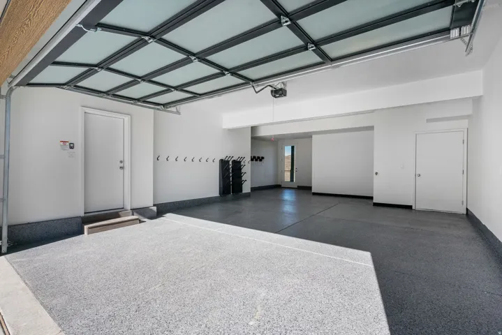 Spacious garage featuring a frosted panel garage door, epoxy floor, white painted walls, and built-in wall hooks