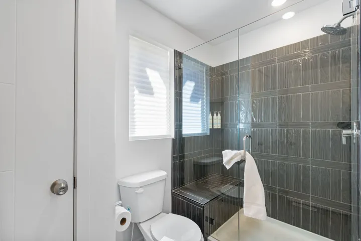Modern bathroom featuring a glass-enclosed shower with dark vertical tile, an integrated shower bench, and a rainfall shower head