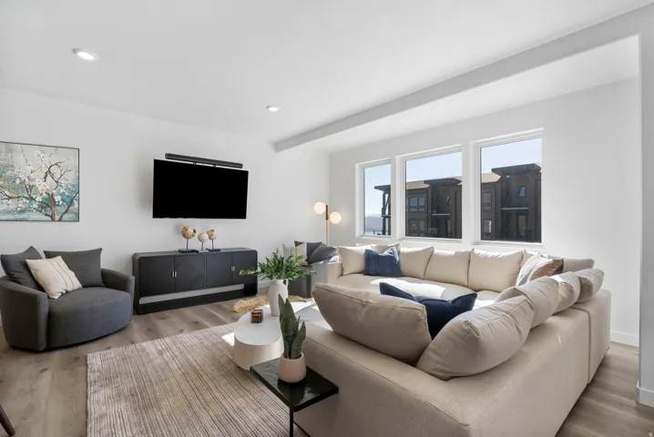 Spacious living area featuring light wood-finish flooring, recessed lighting, and large windows providing ample natural light