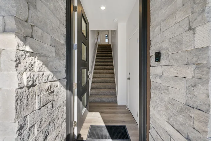 Entryway featuring stacked stone wall details, a contemporary front door with multiple glass panes, wood-finish flooring, and carpeted stairs