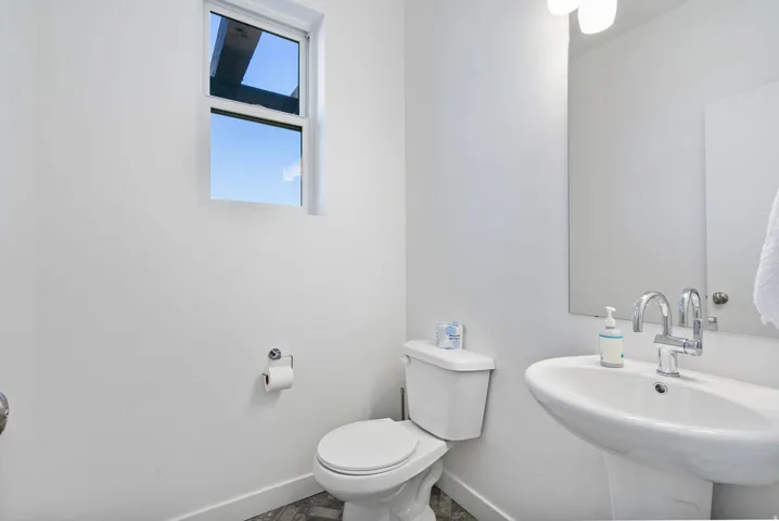 Bathroom featuring a pedestal sink with chrome faucet, a white toilet, and a rectangular window