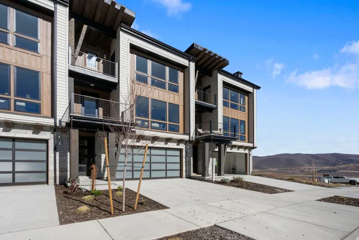 Modern townhome exterior featuring an integrated garage, large windows, multiple balconies, and mixed material siding