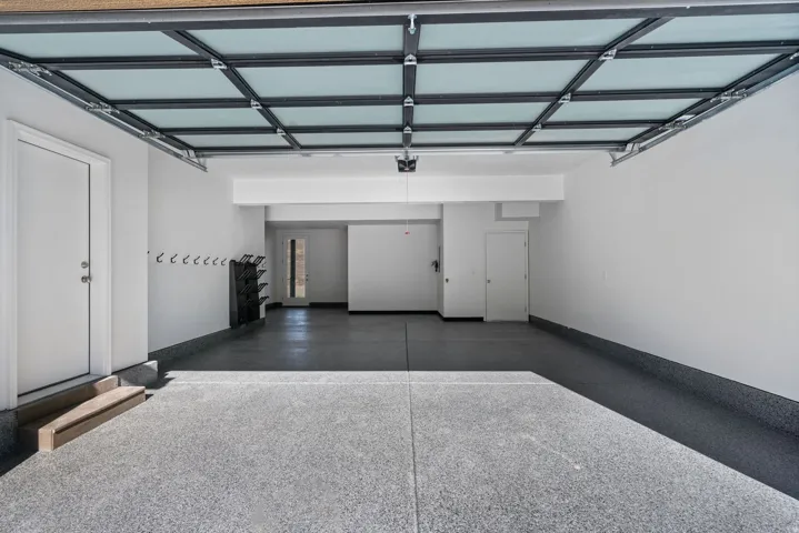 Spacious garage featuring an epoxy floor finish, a translucent panel garage door, white painted walls, and built-in wall hooks