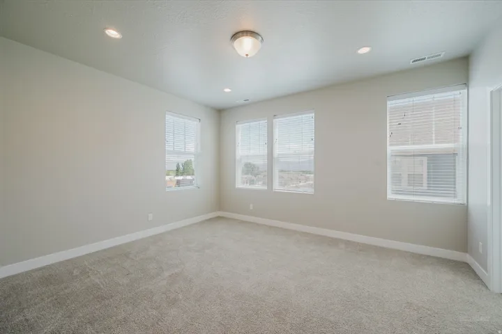 Spacious room featuring neutral carpeting, multiple windows with blinds, recessed lighting, and a flush mount ceiling fixture