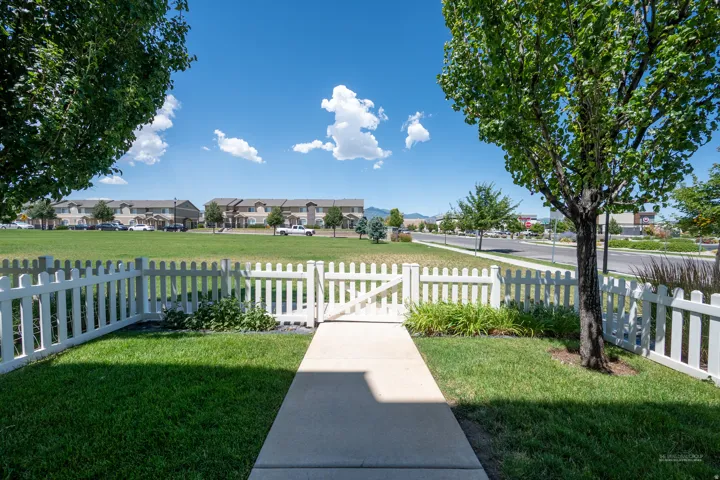 Landscaped front yard featuring a white picket fence, a concrete walkway, and a mature tree