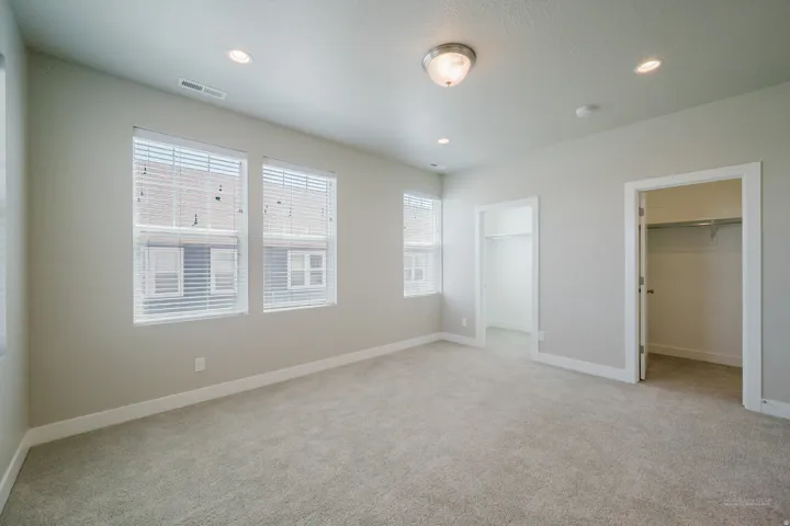 Spacious room featuring light gray carpeting, two windows with blinds, recessed lighting, and a surface-mounted ceiling light