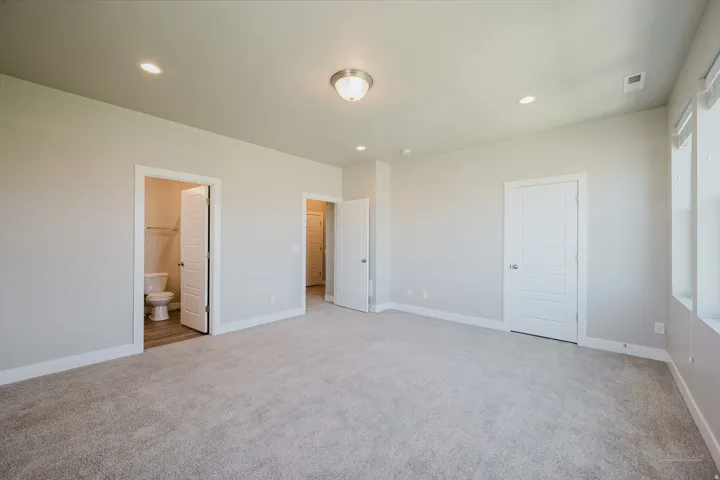 Spacious room featuring plush carpeting, contemporary lighting, multiple doors, and large windows
