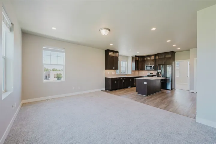 Bright open-concept living area featuring light gray carpeting, multiple windows providing ample natural illumination, and recessed lighting