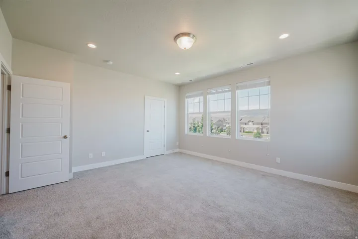 Spacious room featuring three large windows, neutral-toned carpeting, recessed lighting, and a semi-flush mount ceiling fixture