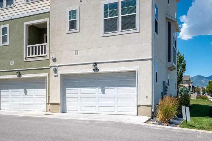 Multi-story stucco and siding exterior featuring two single-car garages, an upper-level balcony with white railings, and multiple windows with horizontal blinds