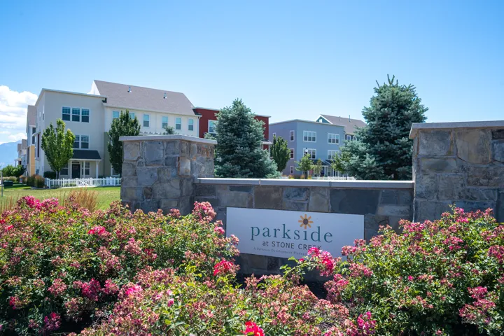 Stone veneer monument sign for Parkside at Stone Creek, surrounded by vibrant pink flowering shrubs and manicured landscaping