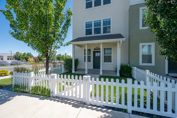Charming front exterior featuring a white picket fence, covered porch entry, mature tree, and landscaping
