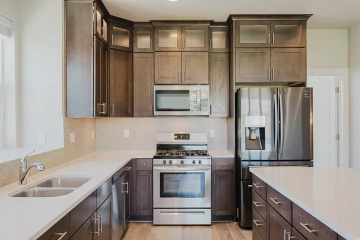 Modern kitchen featuring wood-finish cabinetry, stainless steel appliances, light-toned countertops, a honeycomb-patterned tile backsplash, and wood-finish flooring