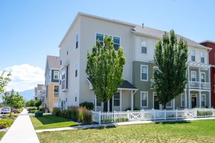 Multi-story townhome featuring a stucco and siding exterior, white picket fence, mature trees, and a covered entry