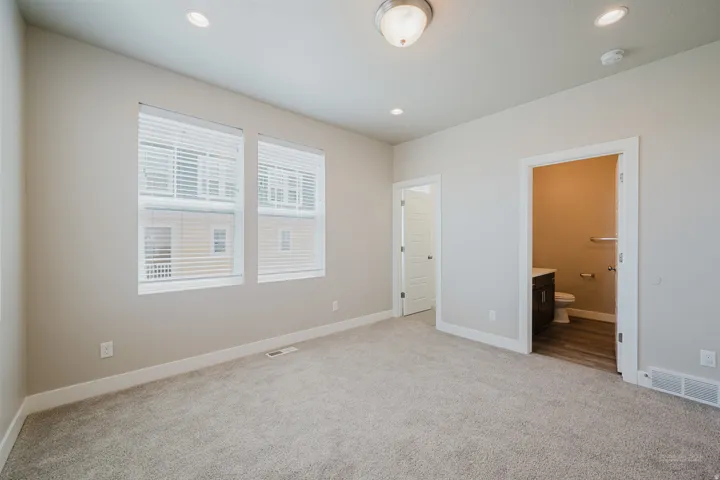 Spacious room featuring neutral carpeting, two large windows with blinds, recessed lighting, and a neutral wall color