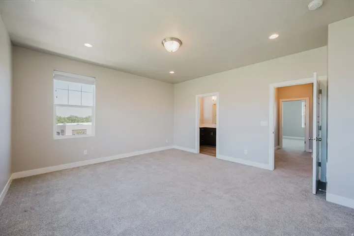 Spacious room with light gray carpeting, recessed lighting, a single window with blinds, and two doorways leading to additional rooms