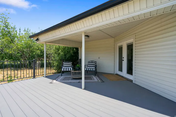 Expansive composite deck featuring a covered patio, dual ceiling-mounted light fixtures, white vinyl siding, and double glass-paneled exterior doors