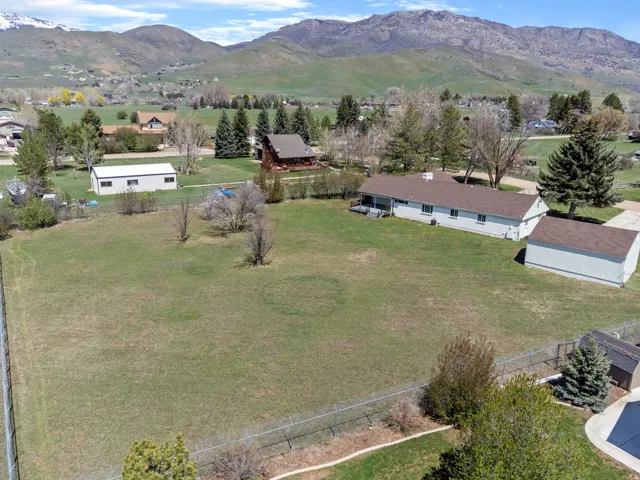 Expansive green lot featuring a single-story residence, a detached garage, and a separate outbuilding, all set against a backdrop of distant mountains