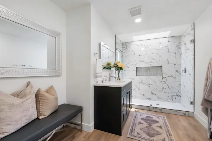 Spacious bathroom featuring a frameless glass shower enclosure with marble-finish tile, an integrated shower niche, and a contrasting dark wood-finish vanity with a light-toned countertop