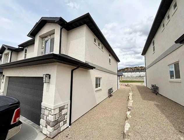 Stucco exterior featuring dark trim, a two-car garage with a panel door, and stone accents