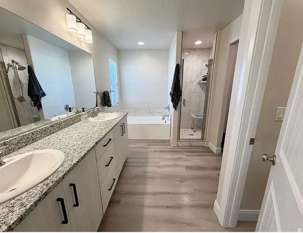 Bathroom with double vanity featuring a speckled countertop, undermount sinks, and light wood-finish flooring