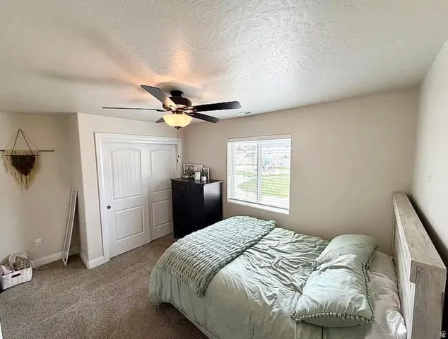 Bedroom featuring neutral wall paint, textured ceiling, a window with blinds, and a built-in closet with paneled double doors