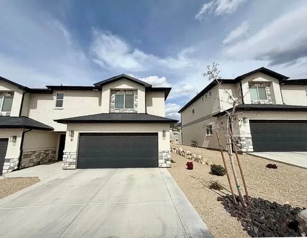 Two-story stucco exterior featuring stone accents, a dark shingle roof, and an attached two-car garage