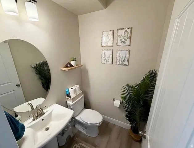 Neutral wall paint and wood-finish flooring complement the white pedestal sink with brushed nickel faucet