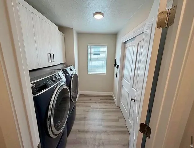 Dedicated laundry area featuring light wood-finish cabinetry with black hardware, wood-finish flooring, a single window with blinds, and white paneled doors