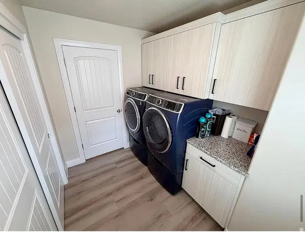 Dedicated laundry space featuring wood-finish flooring, light-toned cabinetry with dark hardware, and a speckled countertop