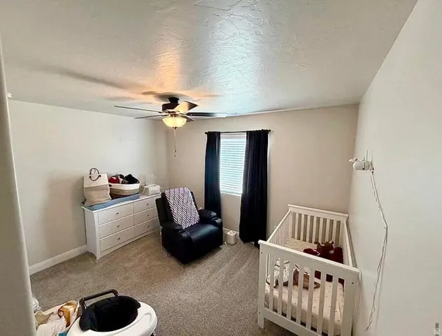 Carpeted bedroom featuring a ceiling fan with integrated lighting, a window with blinds, and neutral painted walls