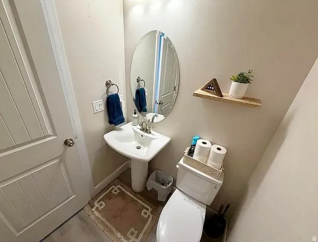 Compact powder room featuring a pedestal sink with a polished chrome faucet, an oval wall-mounted mirror, and a wall-mounted wood shelf