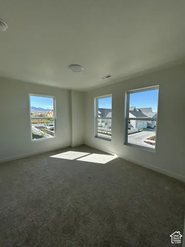 Carpeted room featuring three windows, white walls, and two ceiling-mounted light fixtures