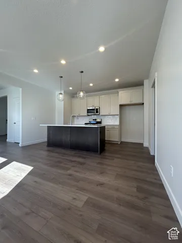 Open-concept kitchen and living area featuring wood-finish flooring, a dark-toned kitchen island with a light-toned countertop, and light-toned upper and lower cabinetry