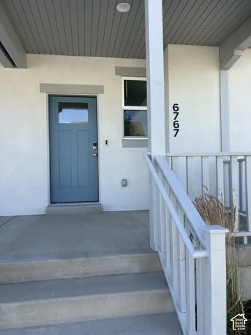 Modern stucco exterior featuring a blue paneled entry door with glass insert, a complementary white trim window, and concrete steps leading to the covered porch