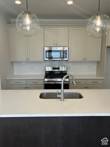 Kitchen island featuring a stainless steel sink, brushed nickel faucet, and light-toned countertop
