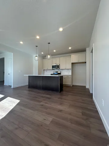 Open-concept kitchen and living area featuring wood-finish flooring, a dark-toned kitchen island with a light-toned countertop, and light-toned upper and lower cabinetry