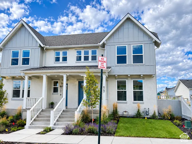 Two-story exterior featuring a mix of vertical board-and-batten siding and textured stucco, covered front porch with white railing, and multi-pane windows