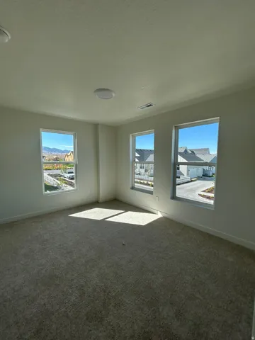 Carpeted room featuring three windows, white walls, and two ceiling-mounted light fixtures